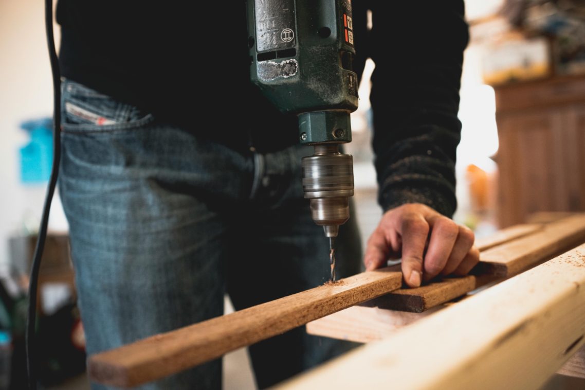 MENUISERIE Un homme utilise une perceuse électrique sur une planche de bois.